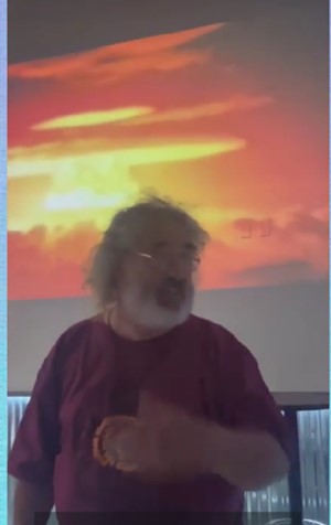 Brian Tyrell speaking in front of an atomic blast's mushroom cloud